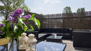 Un espace extérieur aménagé avec une table en verre, des meubles en osier et un vase décoratif orné de fleurs violettes.