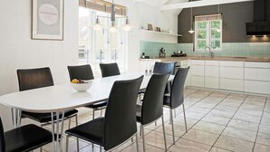 Une cuisine moderne avec des meubles blancs, un grand îlot central et un coin repas comprenant des chaises noires et une table blanche.