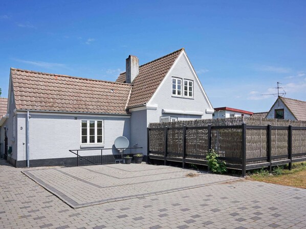 A white house with a tiled roof, a fenced backyard, and a paved driveway.