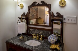 A bathroom with a marble sink, gold faucets, a large mirror, and a towel rack. - The Cottage on Maple (Murfreesboro)