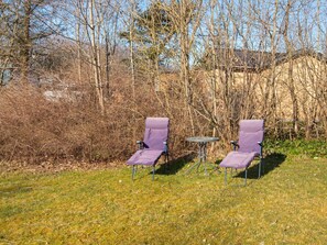 Two outdoor chairs with a small table between them, set on a grassy area with trees in the background. - 4 Person Holiday Home in Nibe (Nibe)