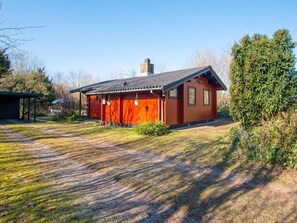 A red wooden cabin with a sloped roof, a chimney, and a small porch area. - 4 Person Holiday Home in Nibe (Nibe)