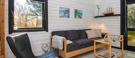 A cozy living room with a dark grey sofa, a black leather chair, a wooden coffee table, and a small shelf with decorative items.