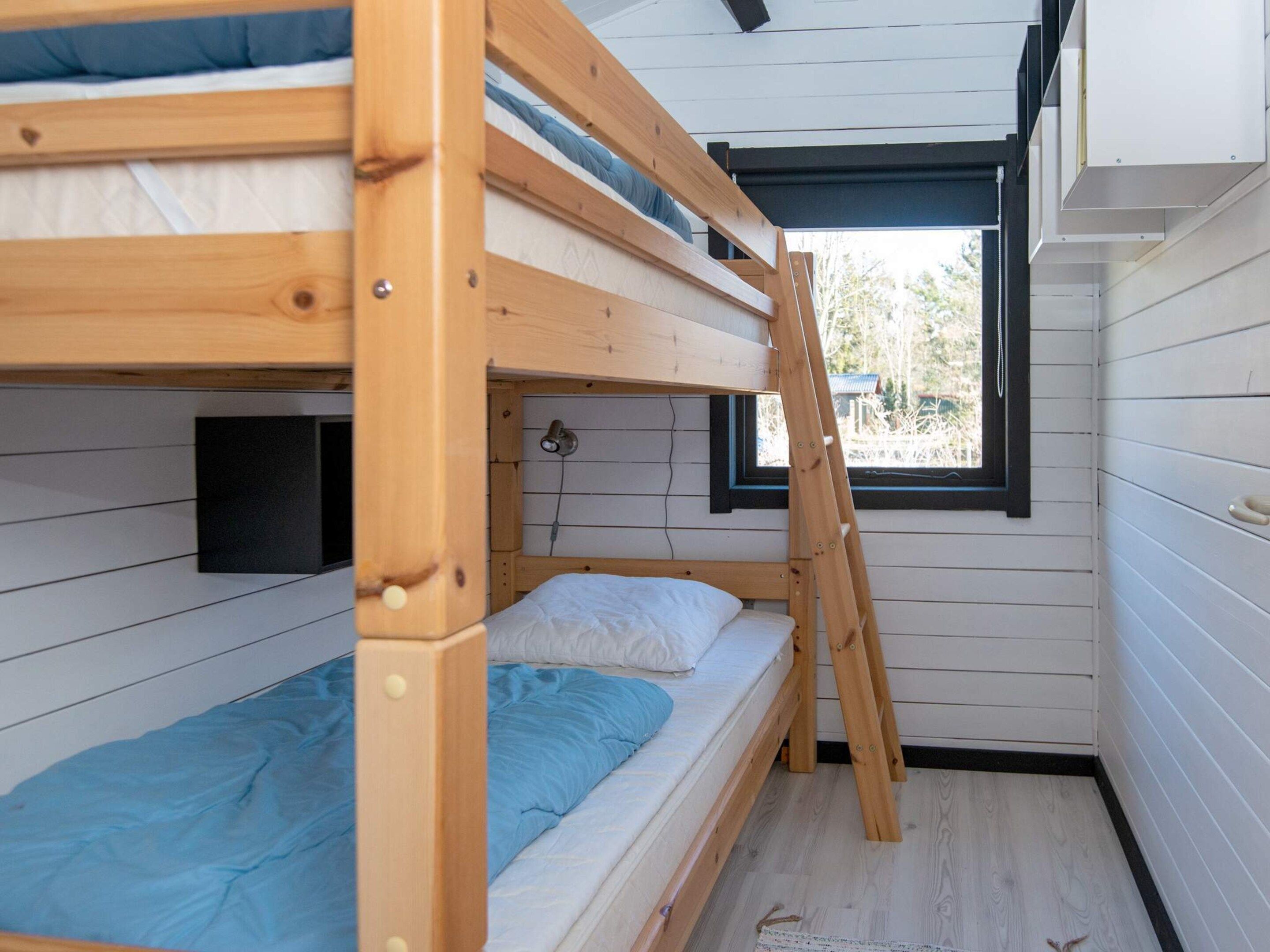 Habitación con literas, una escalera, una ventana y una lámpara en la pared.