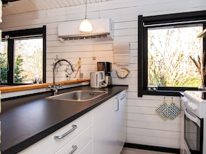 A kitchen with a black countertop, white cabinets, a stainless steel sink, a coffee maker, and a window with a view of trees. - 4 Person Holiday Home in Nibe (Nibe)