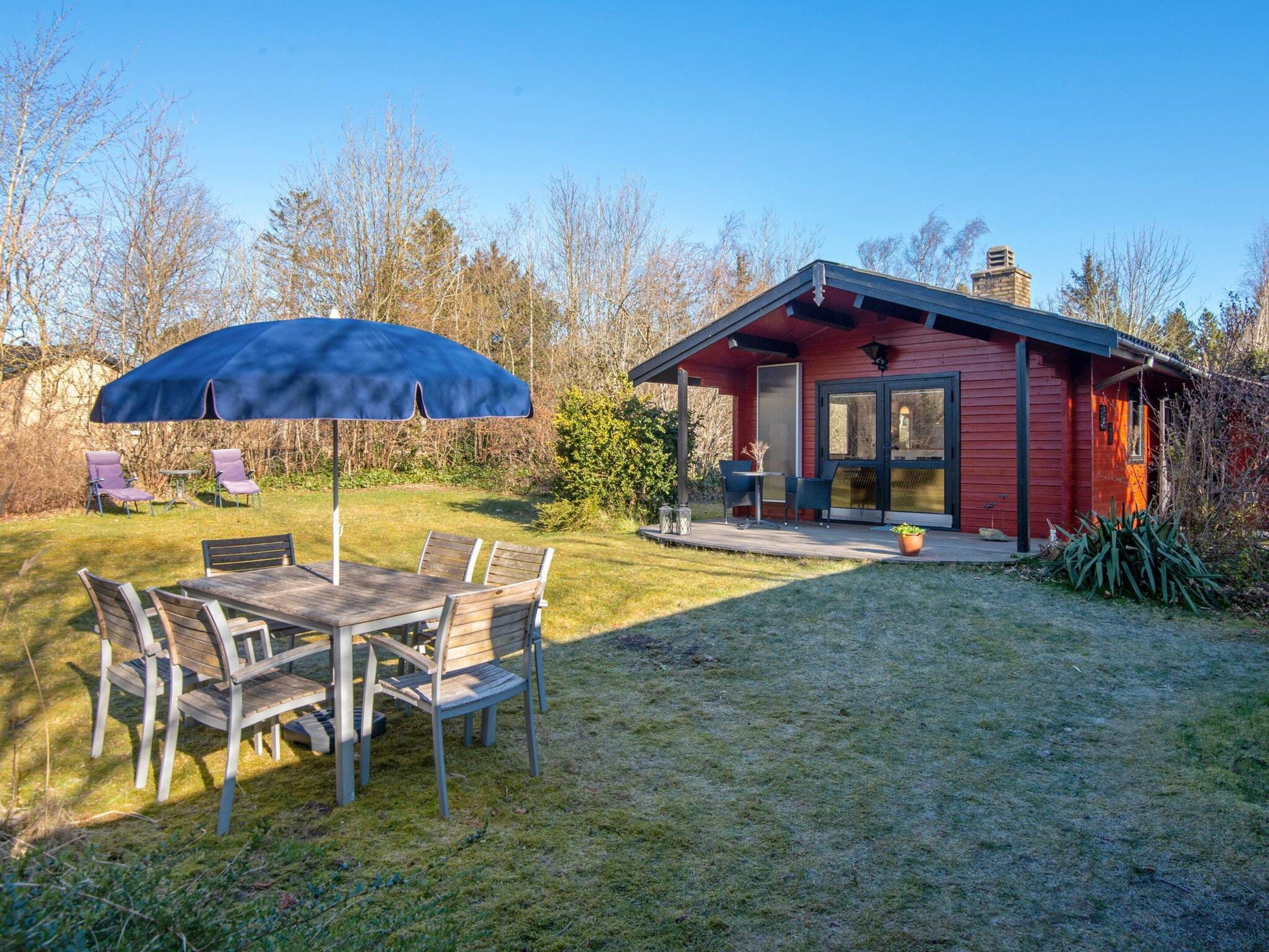 A red cabin with a porch, a dining table with chairs, and a blue umbrella.