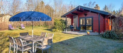 A red cabin with a porch, a dining table with chairs, and a blue umbrella.