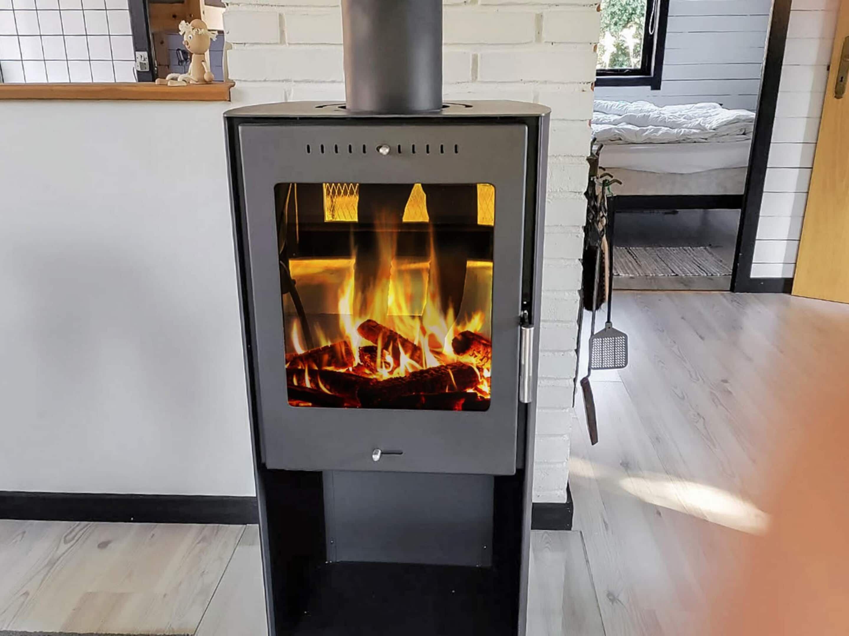 A modern wood-burning stove in a room with a bed and a small table.