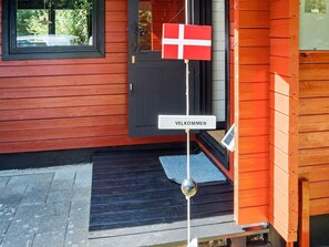 A wooden house with a red door and a welcome sign. - 4 Person Holiday Home in Nibe (Nibe)