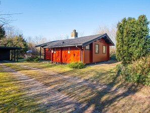 A red wooden cabin with a sloped roof, a chimney, and a small porch area. - 4 Person Holiday Home in Nibe (Nibe)