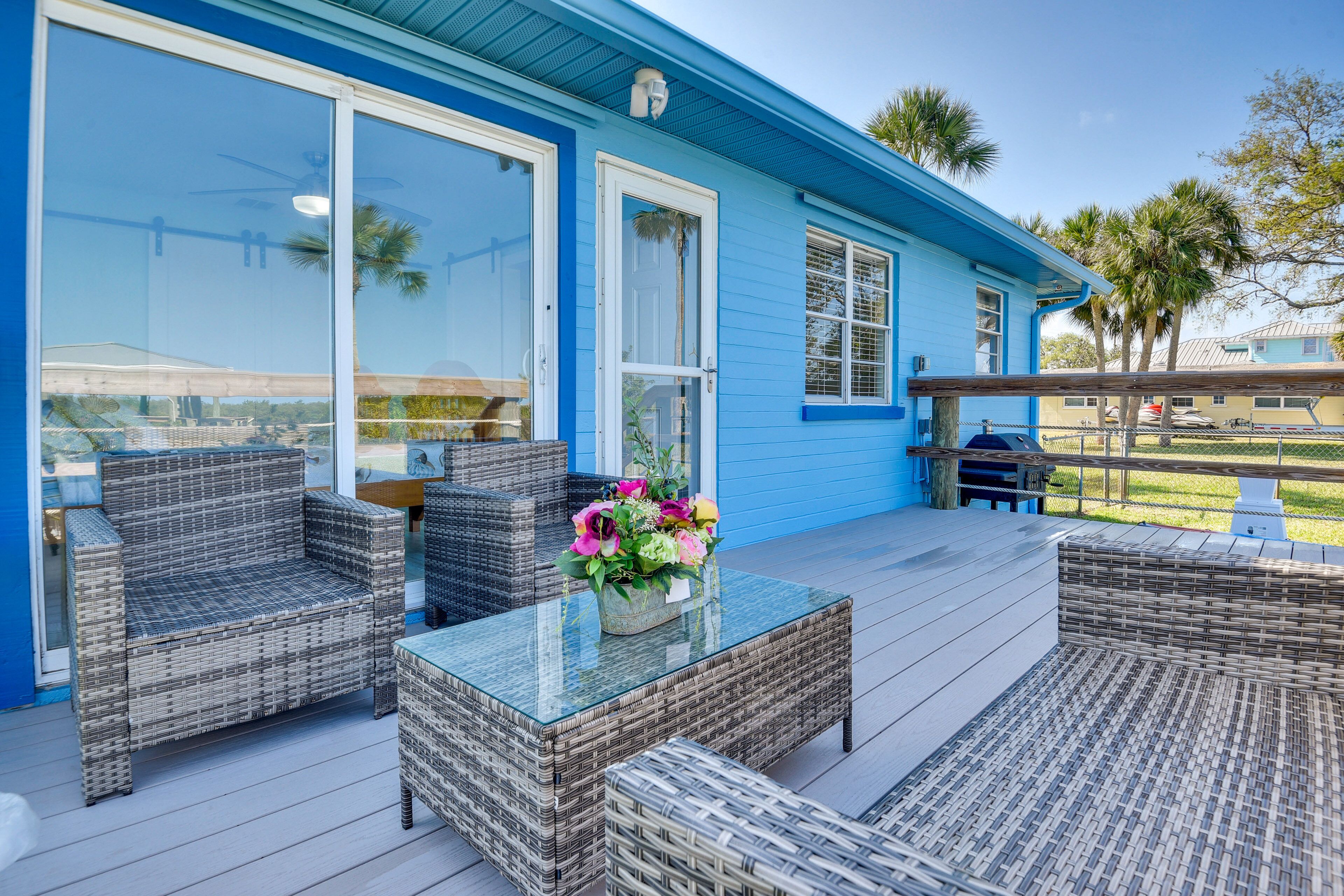 A blue house with a covered patio area featuring wicker furniture and a glass-top table with a flower arrangement.