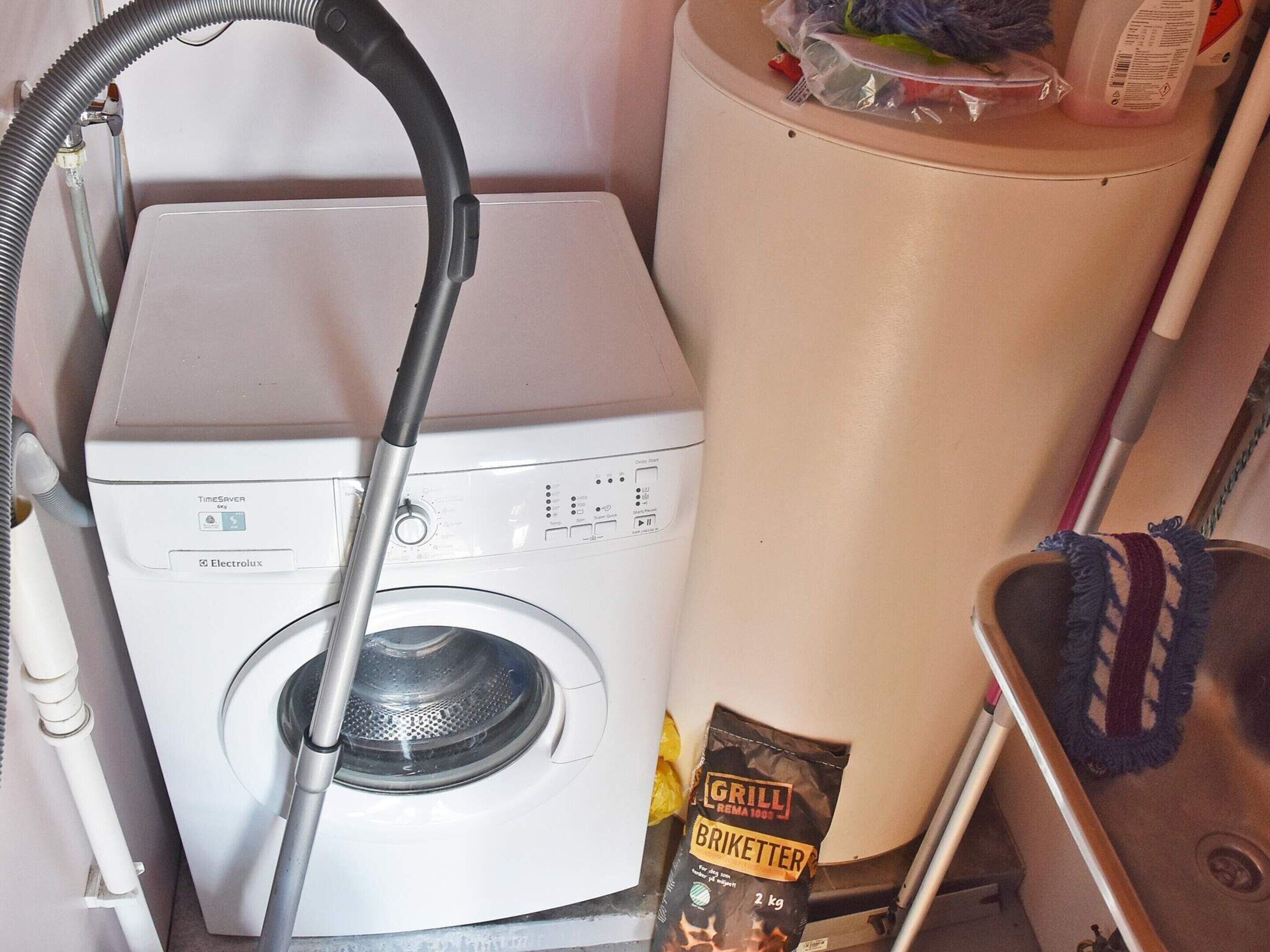 Un appareil compact combinant lave-linge et sèche-linge, muni d’un tuyau, un sac de briquettes pour barbecue et une serpillière dans un évier.