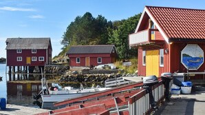 Een kade aan het water met boten, een rood gebouw met een gele deur en een muurschildering aan de zijkant.