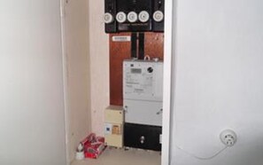 A narrow hallway with a utility room containing electrical equipment and a control panel.