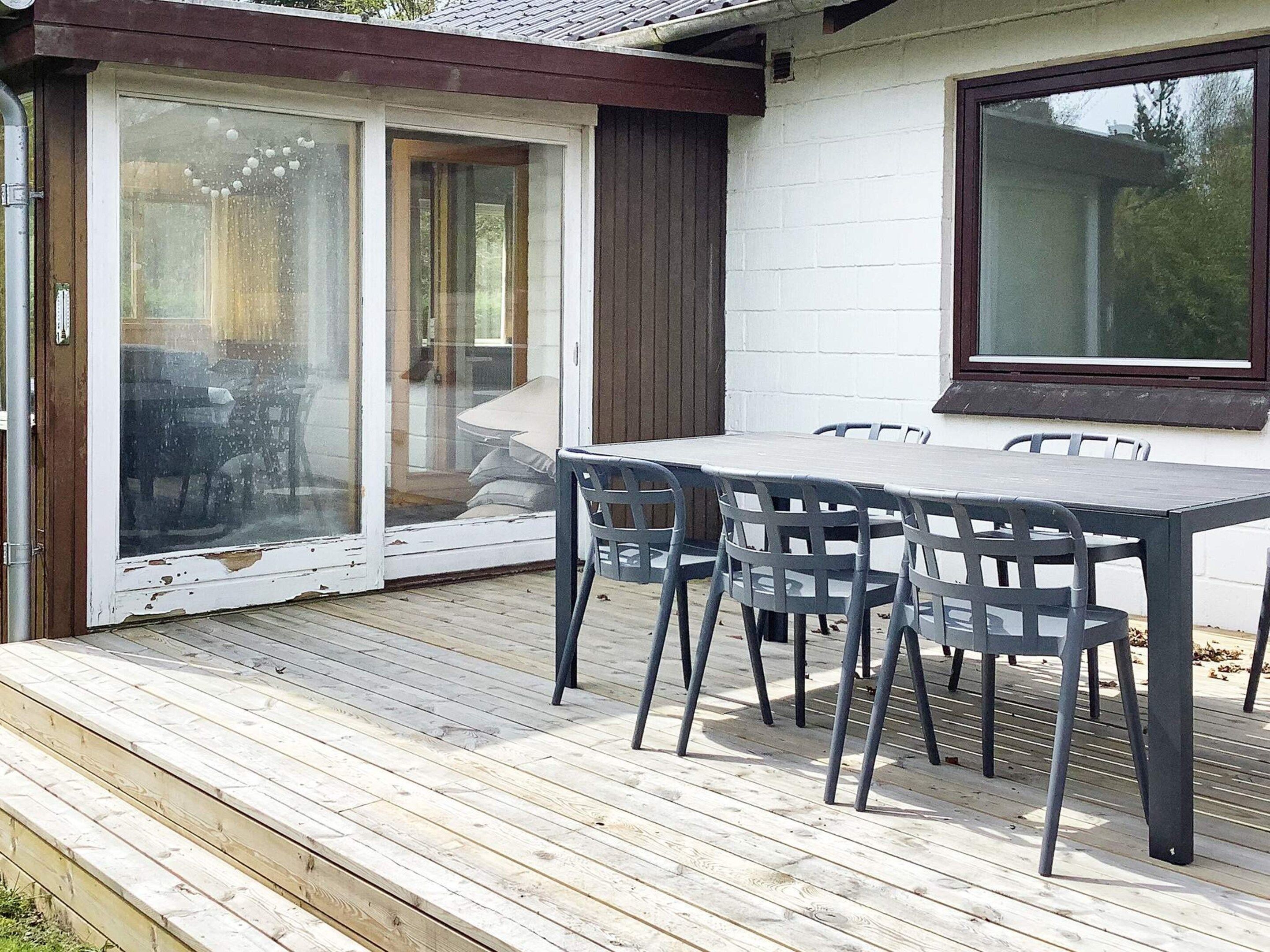 A wooden deck with a table and chairs, a sliding glass door, and a window.