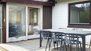 Puisesta laudasta rakennettu terassi, jossa on pöytä ja tuolit, liukuovi ja ikkuna.