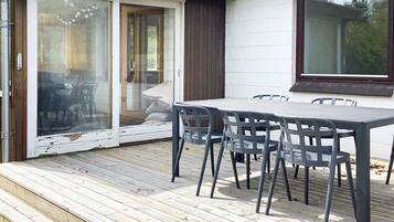 A wooden deck with a table and chairs, a sliding glass door, and a window.