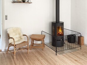 A room with a wood-burning stove, a wicker chair, a wooden table, and a shelf with decorative items.