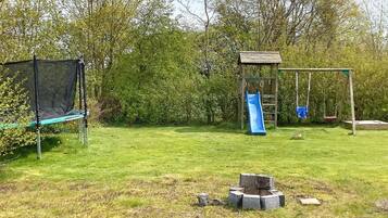 Un parque infantil con columpios, tobogán y cama elástica en un área verde.