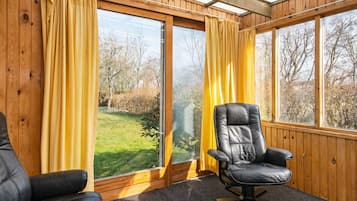 A room with a large window, a black leather chair, and a wooden ceiling.