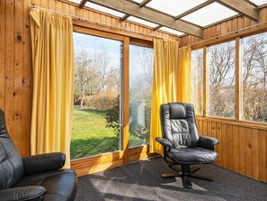 A room with a large window, a black leather chair, and a wooden ceiling.