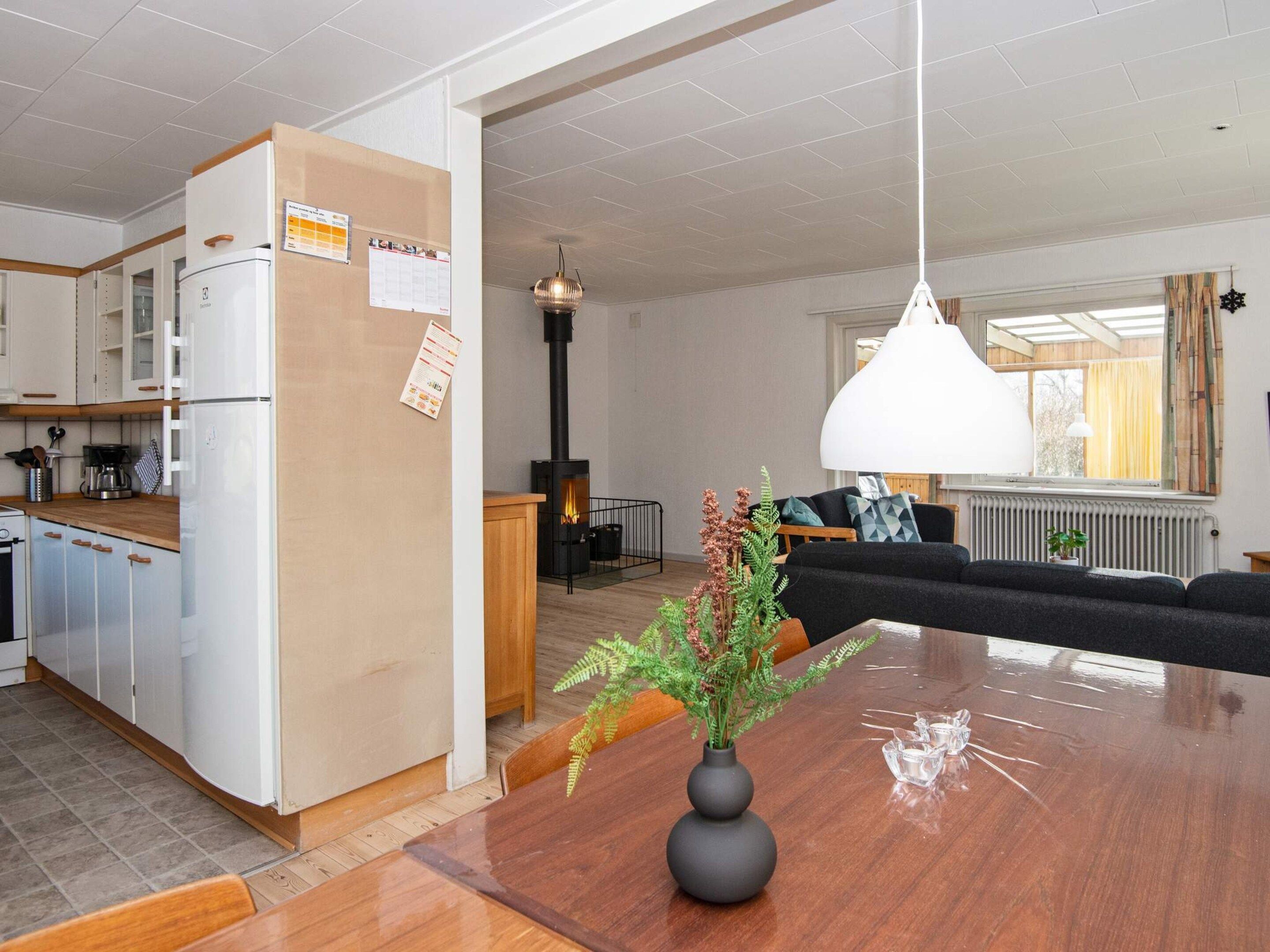 Uma cozinha moderna com geladeira embutida, uma área de jantar com mesa de madeira e uma sala de estar com sofá e lareira.