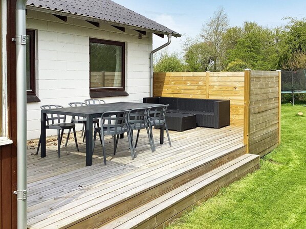 Un patio con terraza de madera, una mesa con sillas y una zona de estar integrada.