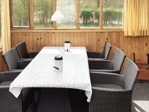A dining area with a table and chairs, a window with curtains, and a hanging light fixture. - 6 Person Holiday Home in Norre Nebel (Norre Nebel)