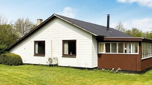 Yhden kerroksen talo, jonka ulkoseinät ovat valkoiset ja koristeet ruskeat. Talossa on kaksi ikkunaa ja savupiippu.