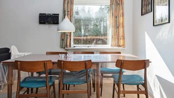A dining area with a table and chairs, a window with curtains, a wall-mounted speaker, and framed pictures.