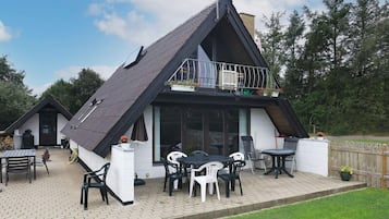 Una casa a due piani con tetto spiovente, un balcone con ringhiera e un patio arredato.