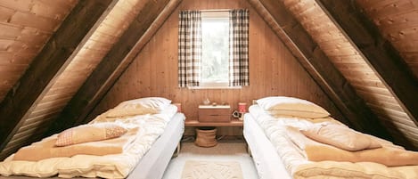 A cozy attic bedroom with two single beds, a small table, and a window with curtains.