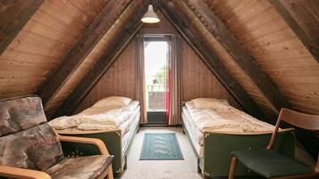 Een knus zolderkamertje met twee eenpersoonsbedden, een houten plafond en uitzicht door een raam.