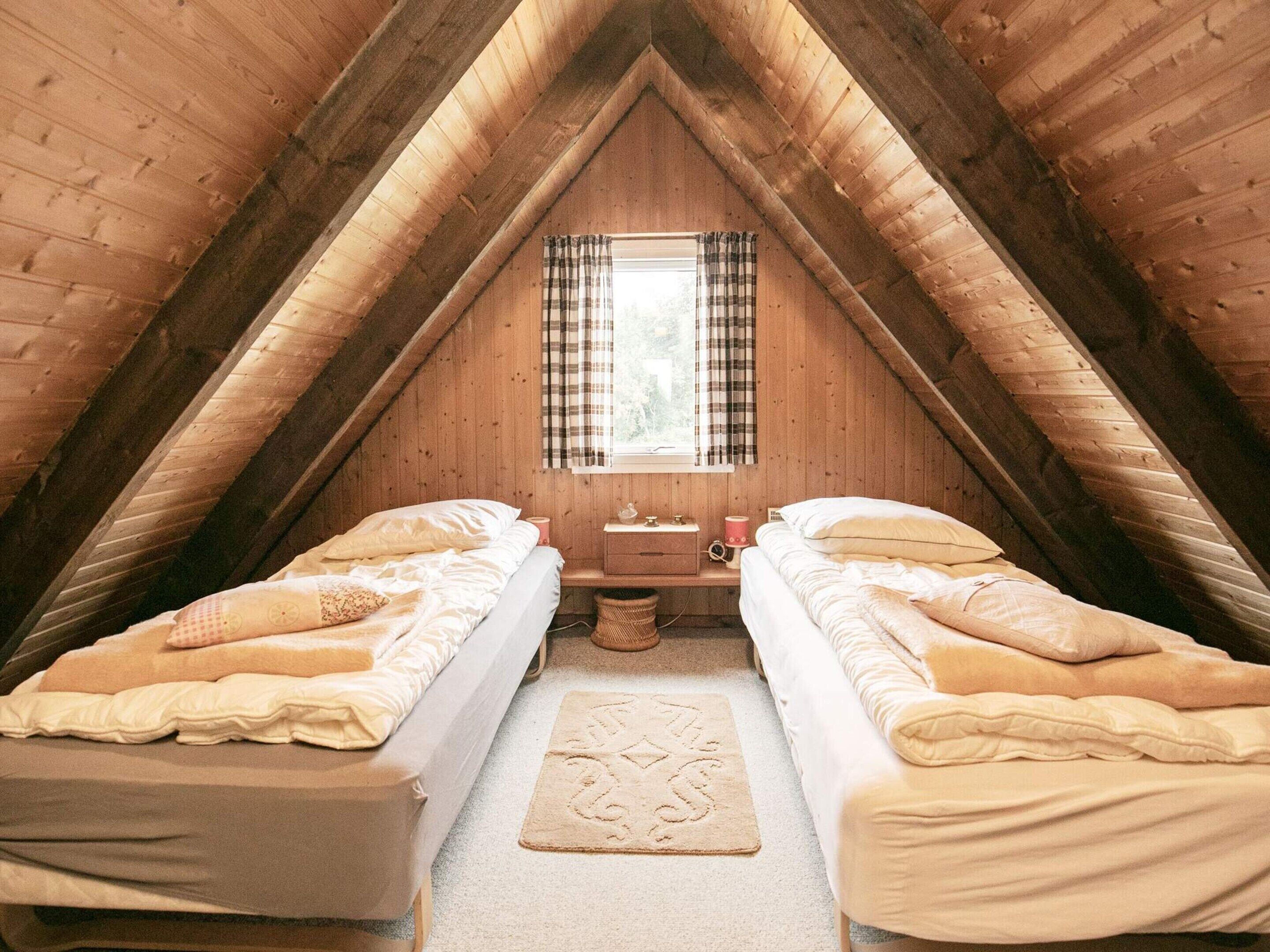 Una camera da letto mansardata accogliente con due letti, un piccolo tavolo e una finestra con tende.