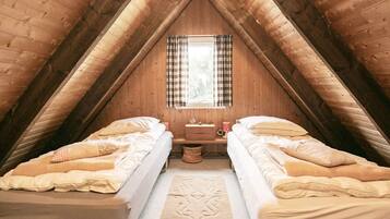 A cozy attic bedroom with two beds, a small table, and a window with curtains.