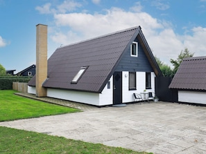 Un edificio residencial con techo inclinado, chimenea y un pequeño patio con mobiliario exterior.