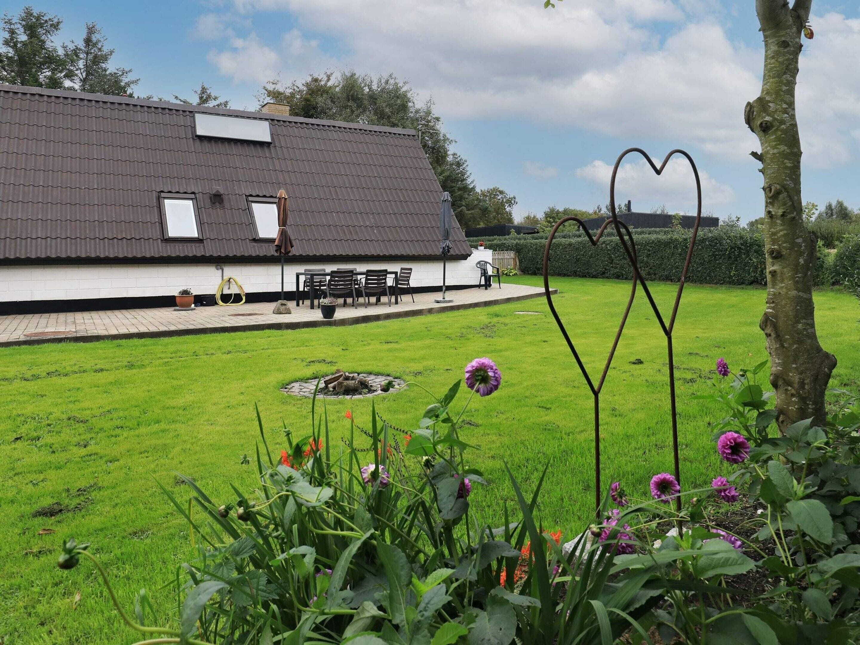 A residential property with a house, a patio with outdoor furniture, and a garden with flowers and a heart-shaped metal sculpture.