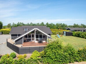 Une maison moderne avec un toit en pente, un patio couvert et un petit espace de jeux équipé d’un toboggan.