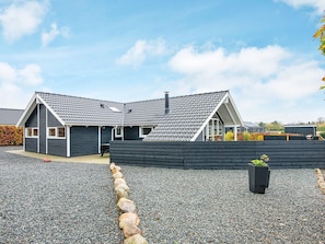 Et moderne hus med skråt tag, en overdækket terrasse og en grusbelagt indkørsel.