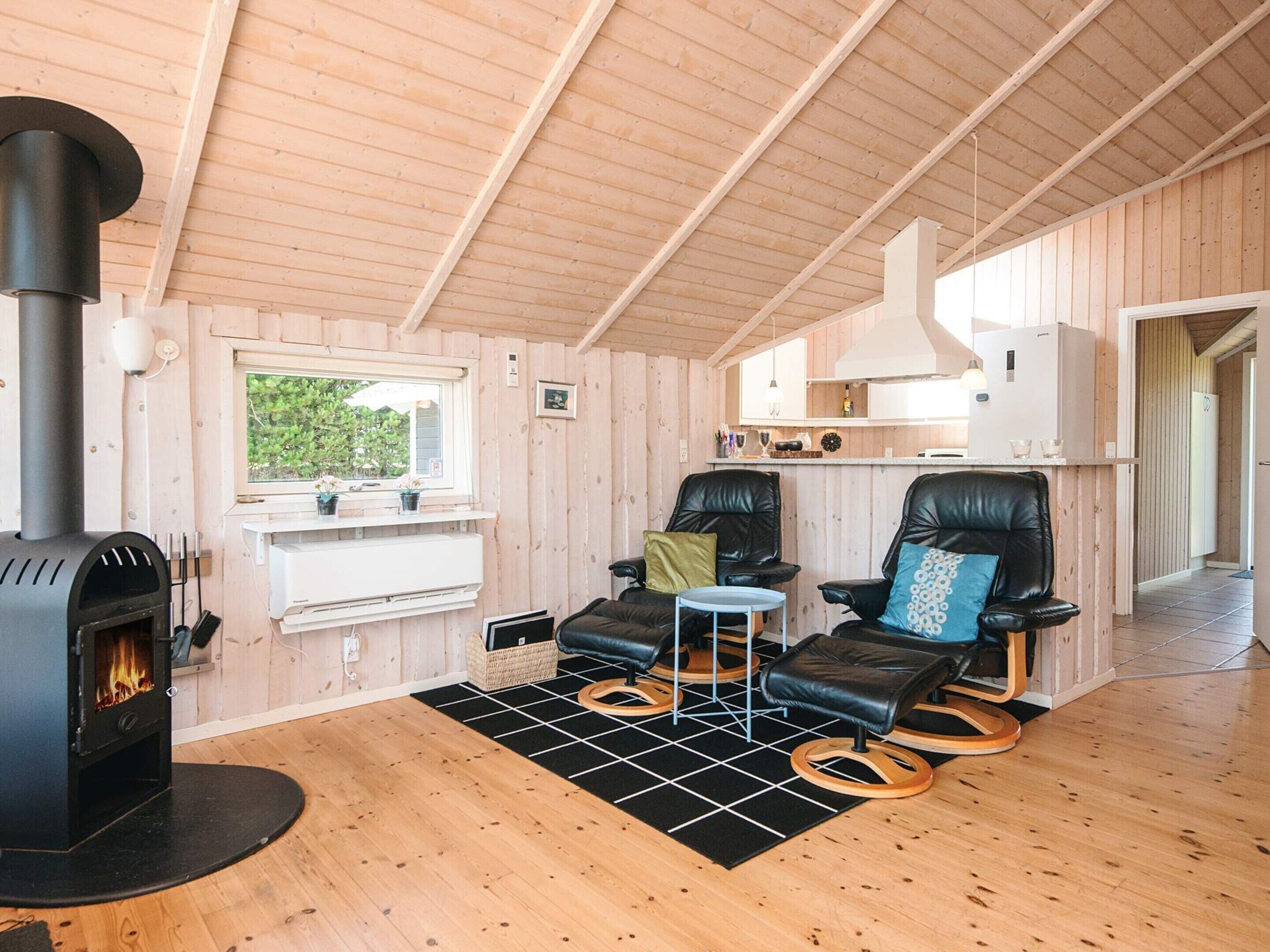 L’intérieur d’un chalet accueillant, avec un poêle à bois, deux fauteuils en cuir, une petite table et une fenêtre donnant sur la verdure.