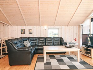 A cozy living room with a black leather sectional sofa, a wooden coffee table, and a television on a stand.