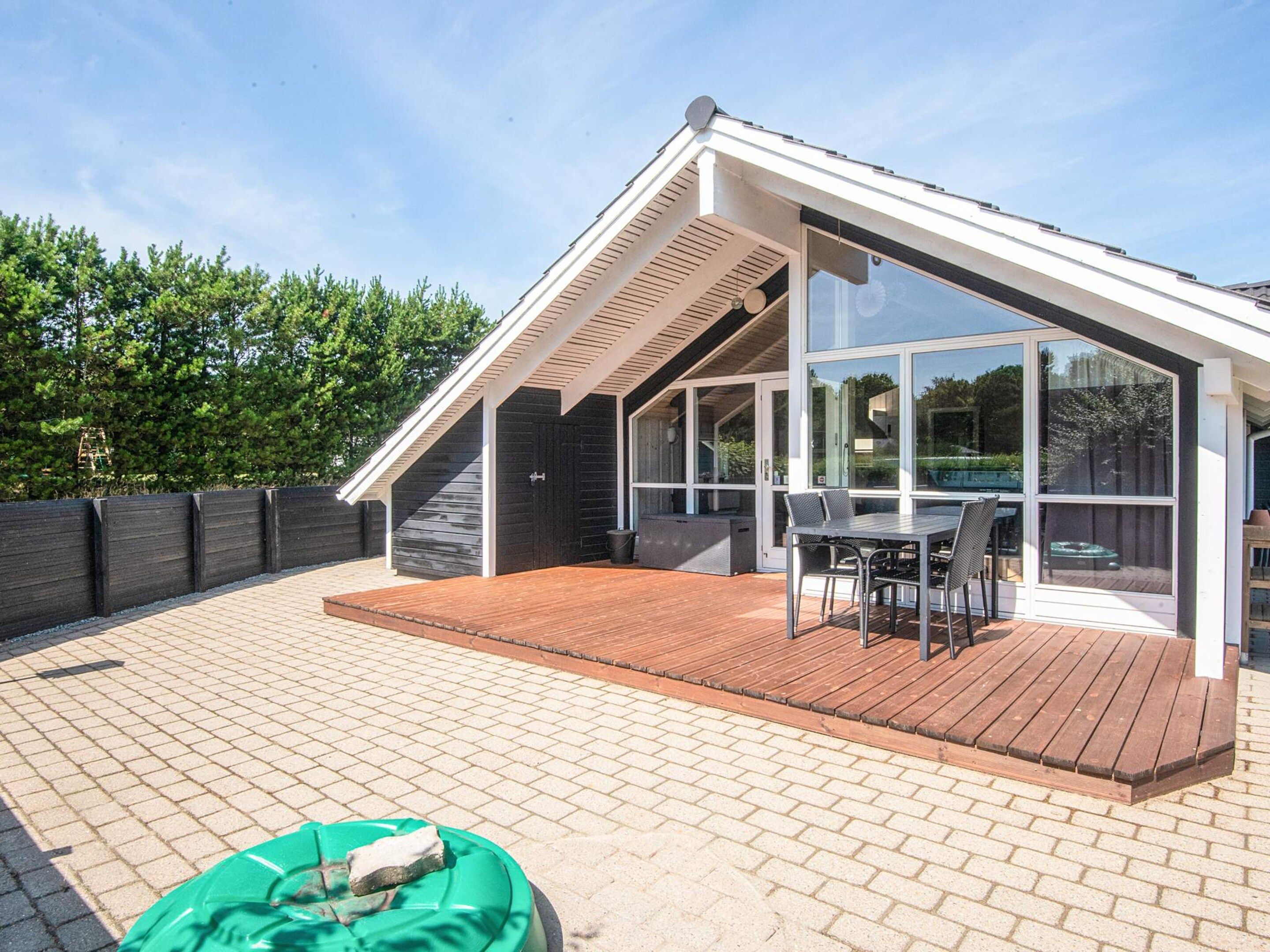 A modern house with a sloped roof, a covered patio with a table and chairs, and a wooden deck.