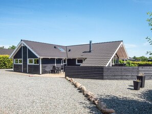 En toetages bygning med et skråt tag, en overdækket terrasse og en grusbelagt indkørsel.