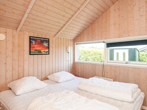 A bedroom with a wooden ceiling, a bed with white bedding, a window with a view of greenery, and a painting on the wall. - 5 Star Holiday Home in Ansager (Ansager)