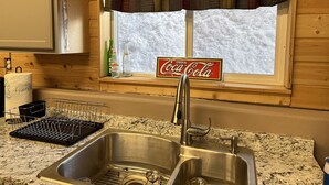 A kitchen with a stainless steel sink, a window with a plaid valance, and a Coca-Cola sign. - The Shabin at Cardiff Spur (Pierce)