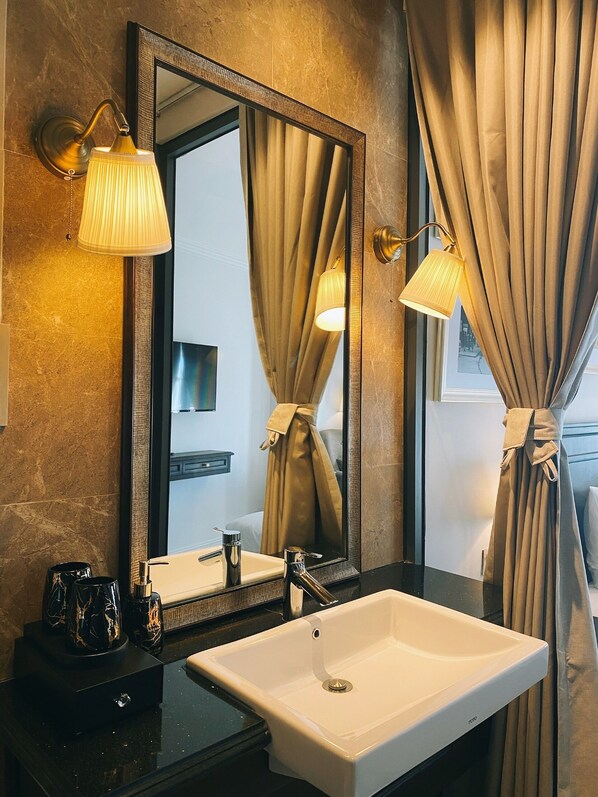 A bathroom with a large mirror, two wall-mounted lamps, a white sink, and a black countertop.