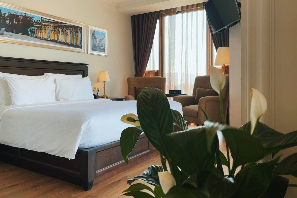 A hotel room with a large bed, a desk, a chair, a television, and a window with curtains.