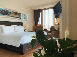A hotel room with a large bed, a desk, a chair, a television, and a window with curtains.