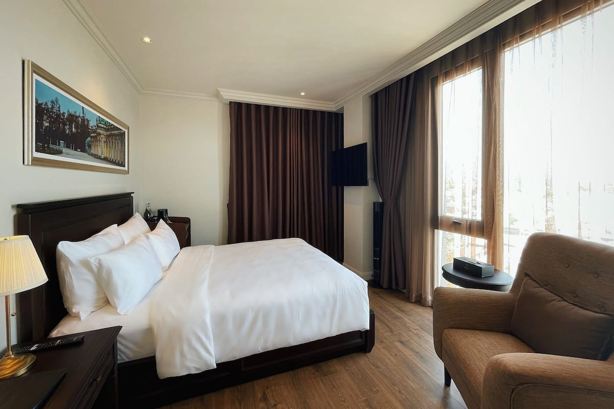 A hotel room with a large bed, a TV, a chair, and a painting on the wall.