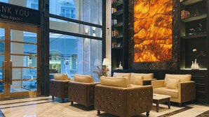 Um hall com um letreiro que diz 'Thank You You Again!', uma grande parede de mármore com efeito de fogo, sofás de couro e uma estante com objetos decorativos.